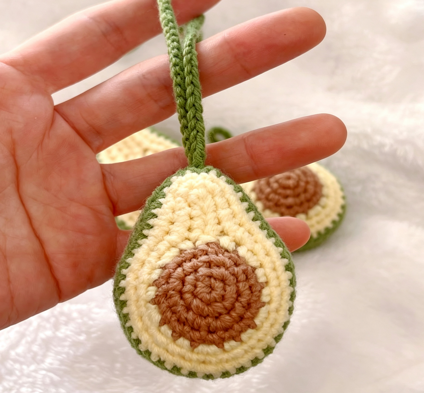 Small crochet avocado keychain hanging on hand for size display