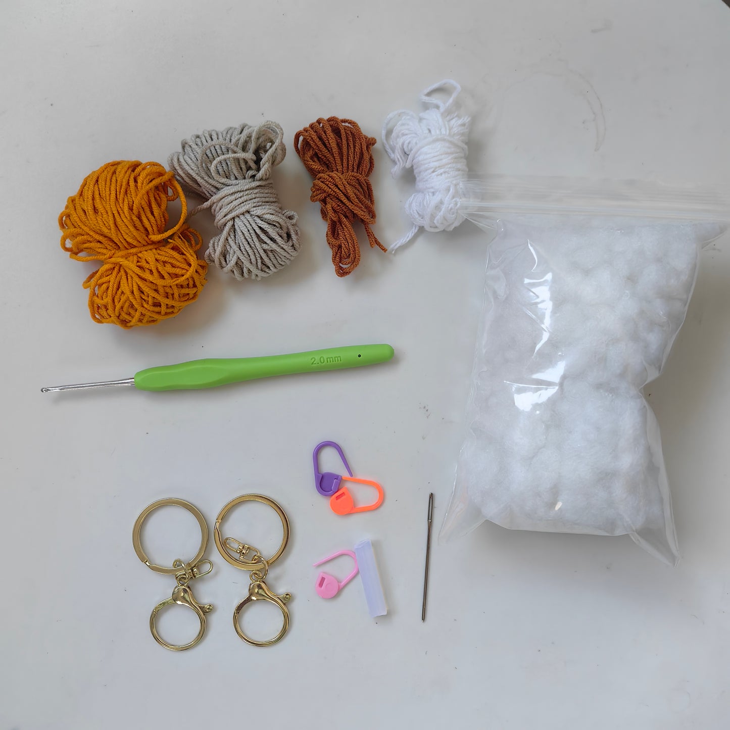 Complete crochet cat plush kit with yarn, crochet hook, stuffing, accessories, and materials for making gray and yellow cat keychains.