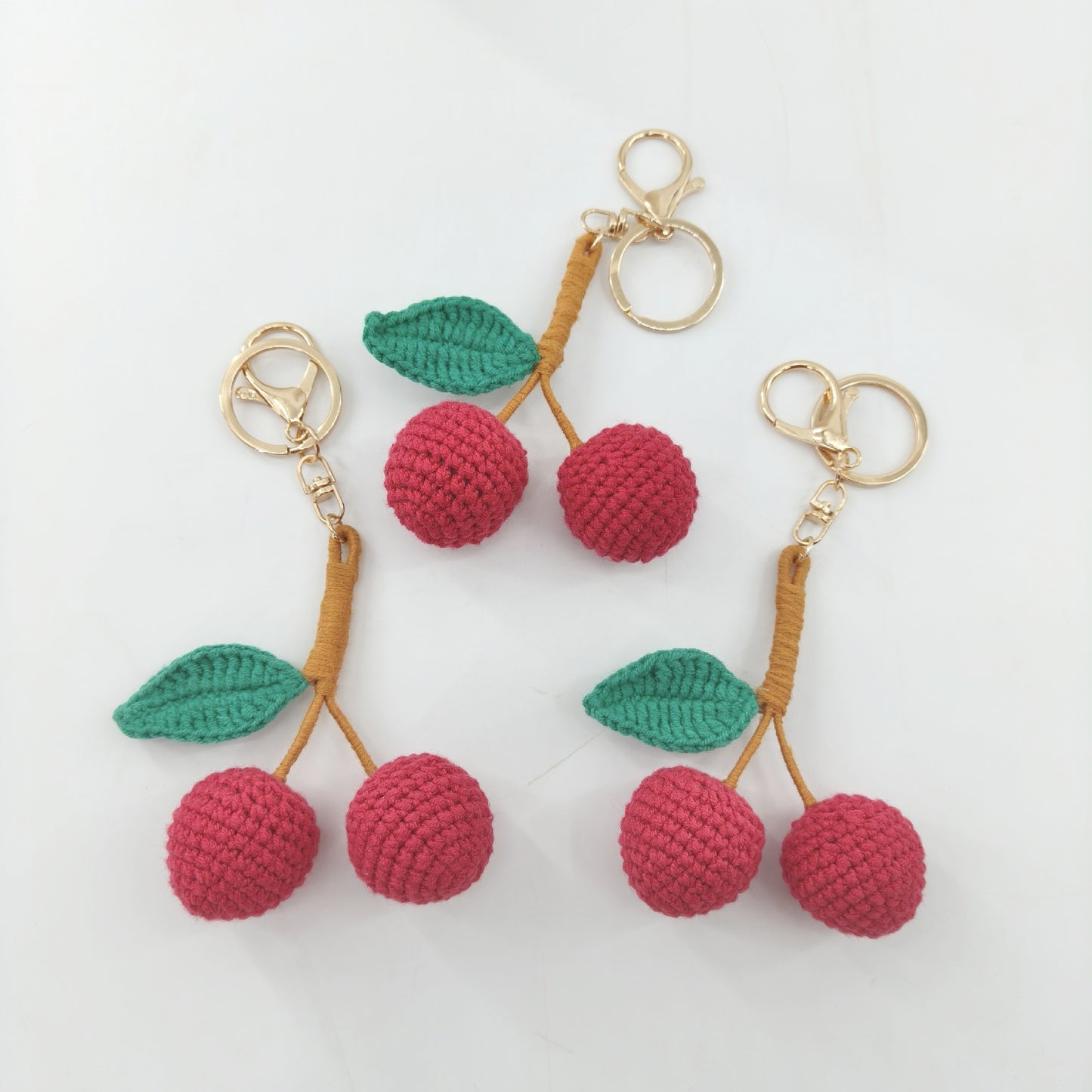 Three cute crochet cherry keychains displayed together, handmade cherry bag charms from Little Loop Crochet.