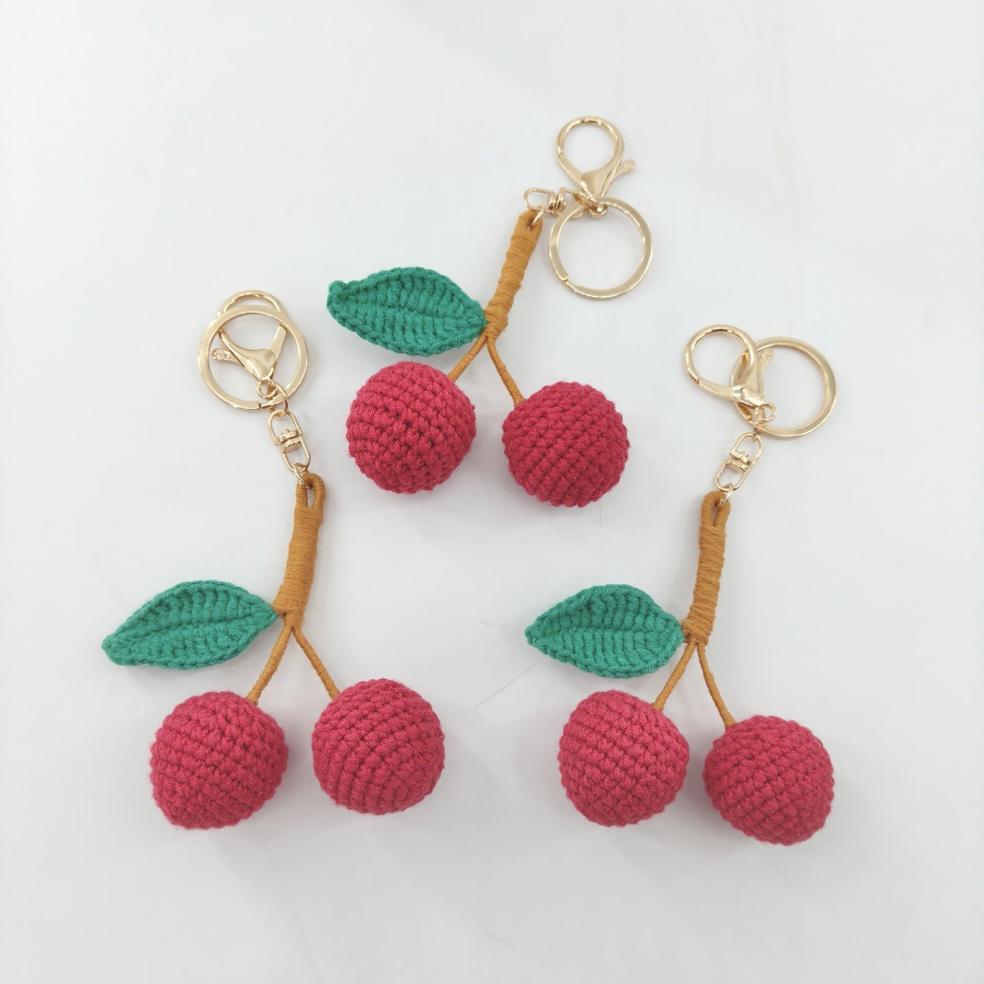 Three cute crochet cherry keychains displayed together, handmade cherry bag charms from Little Loop Crochet.