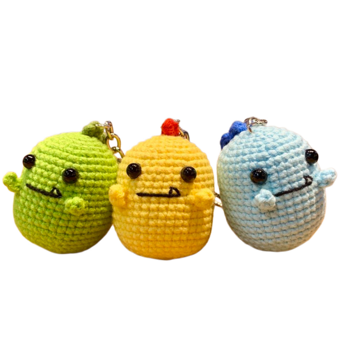 Close-up details of green, yellow, and blue crochet dinosaur keychains