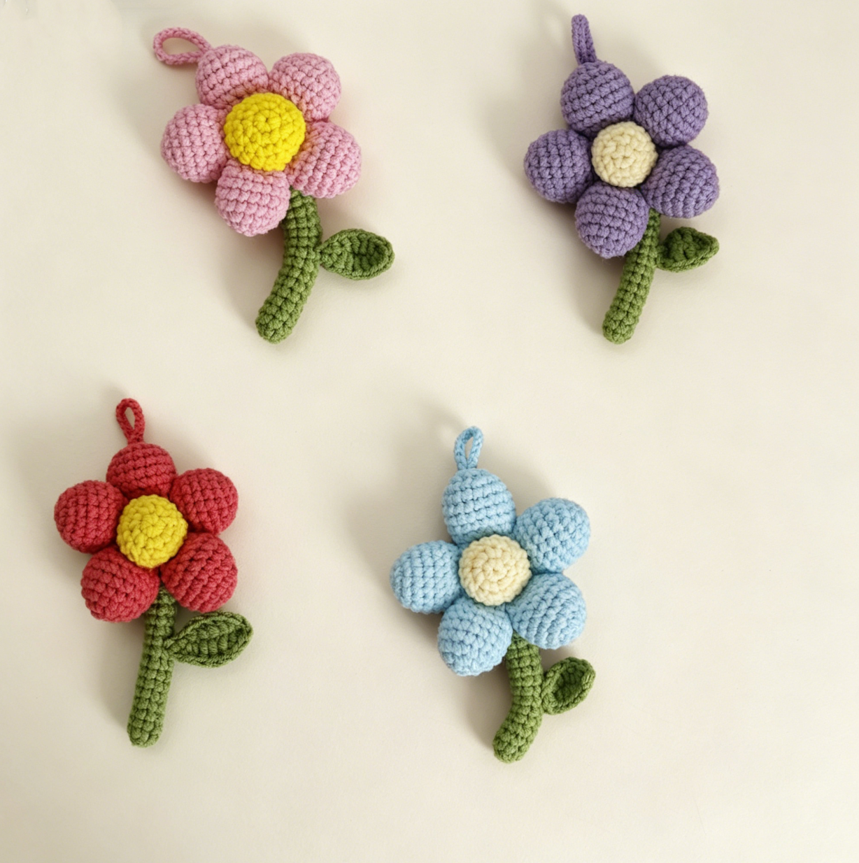 Four colorful crochet flower keychains in pink, blue, purple, and red displayed together